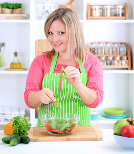 幸福微笑的女人在厨房里准备蔬菜沙拉