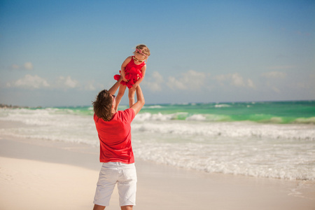 年轻快乐的爸爸和小女儿在白色的沙滩上尽情的在阳光明媚的日子