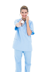 逗乐的护士在玩弄她的听诊器的蓝色磨砂