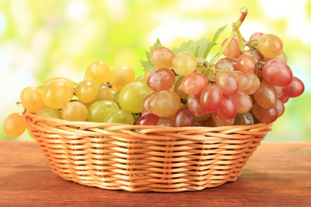 在木桌上，自然背景上的篮子里成熟甜葡萄