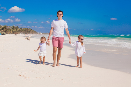 快乐的父亲和他可爱的小女儿，在阳光明媚的日子走在白色的沙滩上