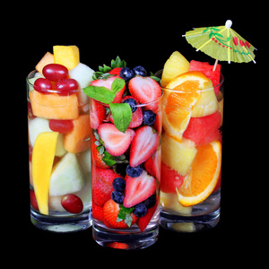 水果鸡尾酒在黑色的背景。新鲜薄荷和伞在顶部用玻璃不同的水果片。健康饮料