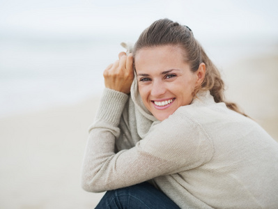 幸福的年轻女人，穿着毛衣坐在海滩上的肖像