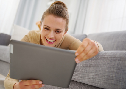 微笑着放在沙发上时使用 tablet pc 的年轻女子
