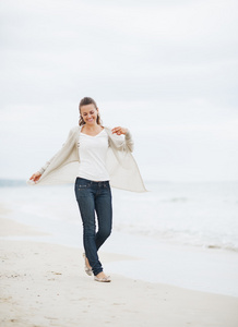 微笑的年轻女子，穿了件毛衣行走在孤独的海滩上