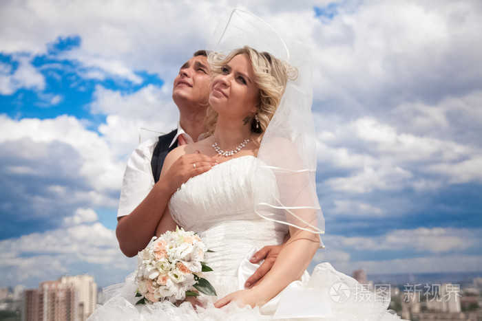 拥抱对蓝蓝的天空和城市景观的已婚的夫妇
