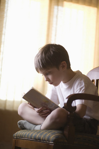 男孩盘腿坐在椅子上看书图片