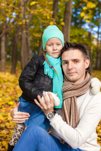 年轻的父亲和他可爱的女儿在秋天公园散步的肖像