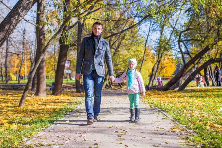 可爱的小女孩，用快乐的父亲走在秋天的公园在晴朗的一天