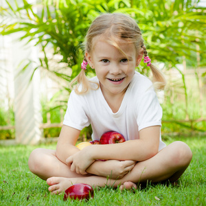 小女孩坐在草地上，抱着苹果