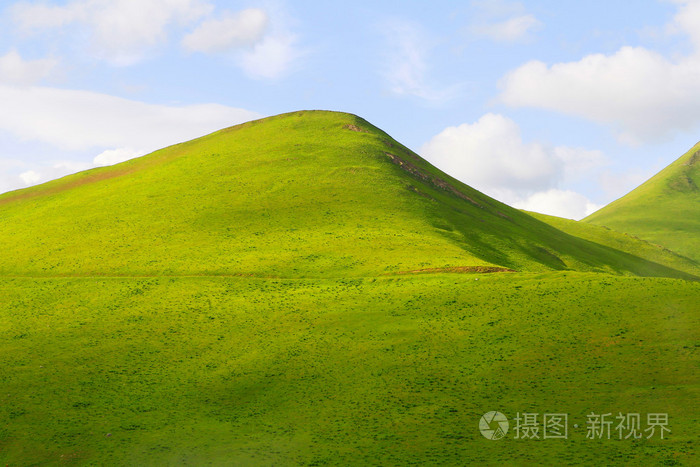 蓝色的天空映衬山上的绿色草地