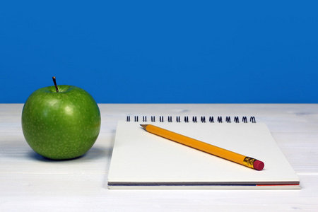 青苹果和用铅笔在白色的木桌上的笔记本