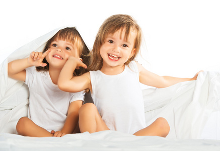 快乐小女孩双胞胎妹妹躺在床上在毯子有之下