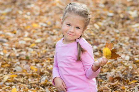 可爱的小女孩玩在秋天公园与五颜六色的树叶