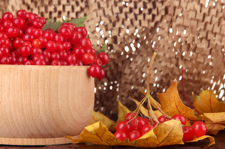 红色浆果的荚蒾在黄色的树叶上棕色背景表格的木碗