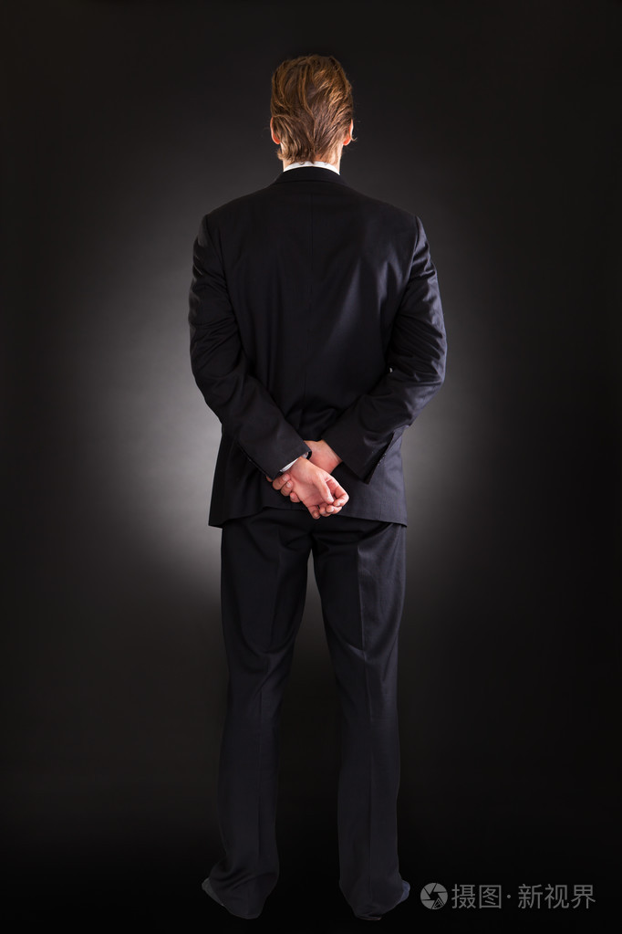 商人用双手背后站立在黑色的背景照片-正版商用图片1drnk4-摄图新视界