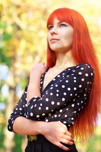 红色的头发站在一个公园在秋天的漂亮女孩