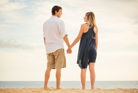 浪漫幸福的夫妇在日落时的海滩上。微笑，手牵着手