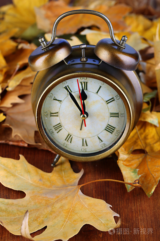 老钟在秋天的落叶在木桌特写