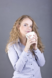 可爱的金发女郎，有着卷曲的头发，从白色的杯子喝喝茶还是喝咖啡