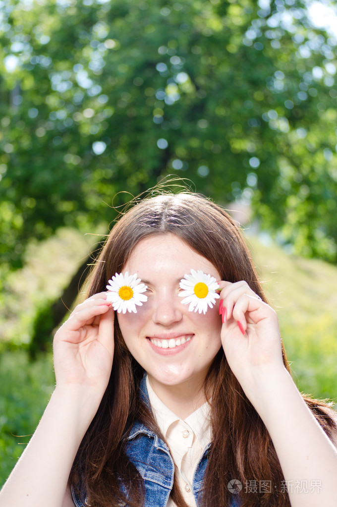 滑稽的青少年女孩雏菊花拿在手在她的眼睛