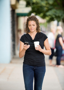 在人行道上使用智能手机的咖啡杯里的女人