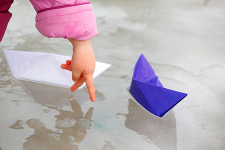 两个纸船在水坑和孩子的手