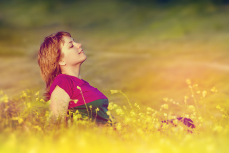 漂亮的年轻女孩，在日落时分坐在草地上享受