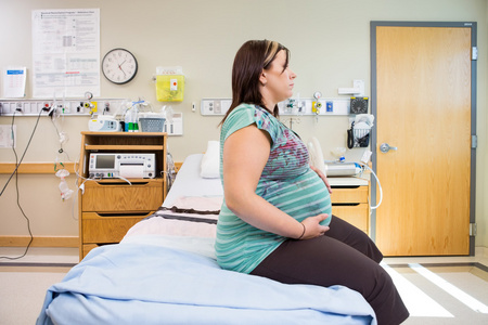 怀孕的妇女，手放在肚子上医院的床上