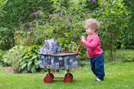 有趣的女婴和老式娃娃推车在花园里