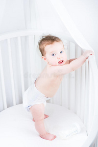穿着尿布的可爱婴儿站在婴儿床上