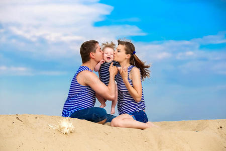 幸福的家庭，妈妈，爸爸，还有穿着条纹背心的小儿子在蓝天背景下的沙滩上玩得开心。夏天