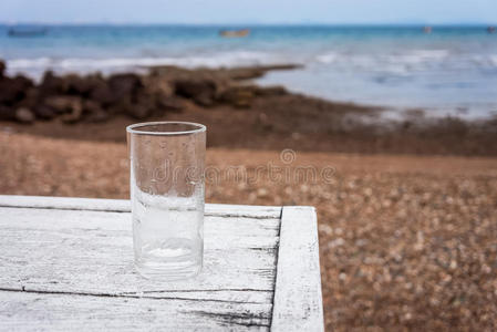 沙滩上的白色木桌上放着一杯空的水