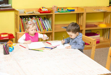 两个小朋友在桌边用彩色铅笔画画。幼儿园男女生画画