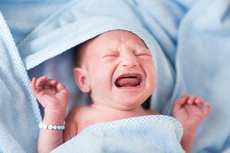 刚出生的婴儿洗澡后用蓝色毛巾哭泣