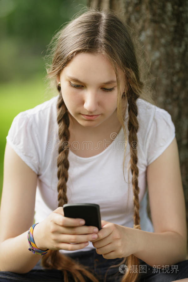坐在树旁拿着手机的少女