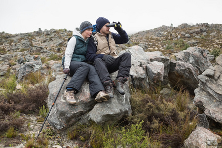 夫妻坐在岩石上用双筒望远镜在一次徒步旅行上