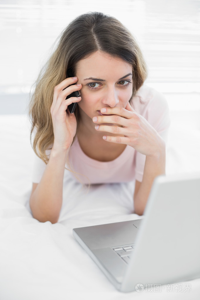 打电话与智能手机躺在她床上的年轻女子