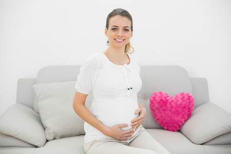 可爱的孕妇自豪地微笑着坐在沙发上的照相机