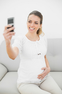 有吸引力的微笑孕妇服用与她的智能手机的自画像