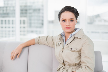 严重衣着光鲜的女人坐在家里的沙发上