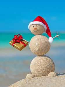在金色的礼物的圣诞帽子海滩沙质的笑脸雪人
