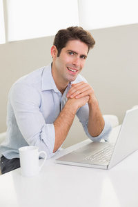 休闲的男人微笑着在家里使用便携式计算机