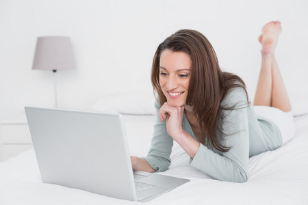 轻松休闲的微笑女人在床上使用笔记本电脑