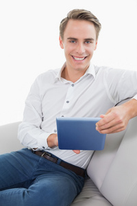 在沙发上使用数字平板电脑的年轻男人休闲微笑着