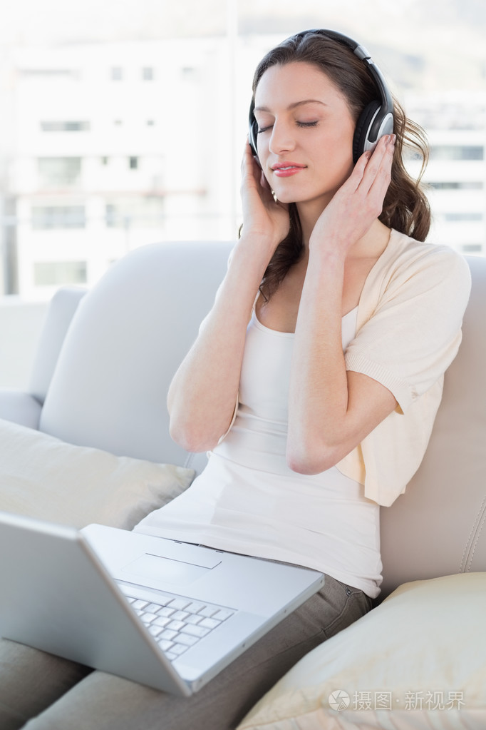 放松的女人坐在沙发上的音乐欣赏的笔记本电脑