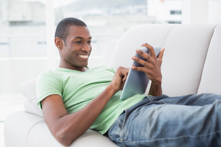 在沙发上使用数字平板电脑的黑人男人休闲微笑着