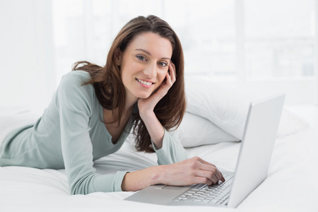 轻松休闲的微笑女人在床上使用笔记本电脑