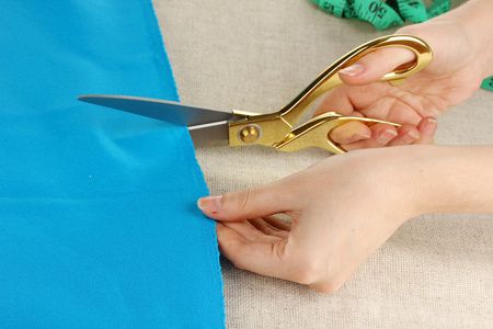 女裁缝师剪蓝色的布米色织物背景上