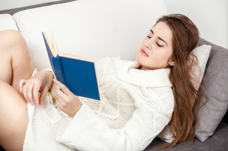 聪明的女人，穿着白色的毛衣躺在沙发上，看书